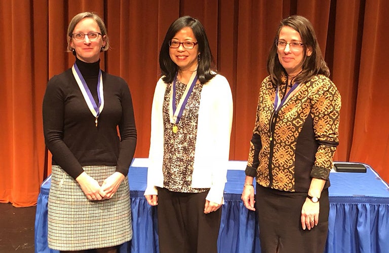 Professors Jennifer Fox, Amy Liu, and Sarah Stoll pose with the Dean's Award medals against a red backdrop.