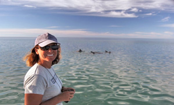 Prof. Janet Mann poses with dolphins in a bay in the background 