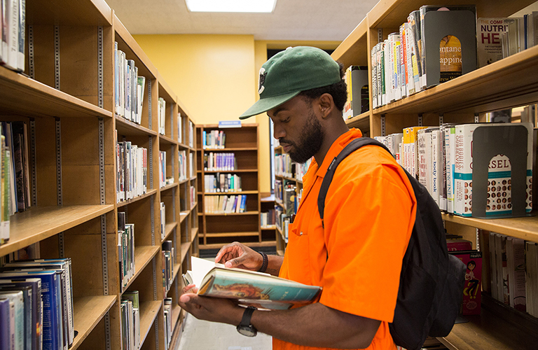 Sherrill Roland reads a magazine in a library while wearing an orange prison jumpsuit