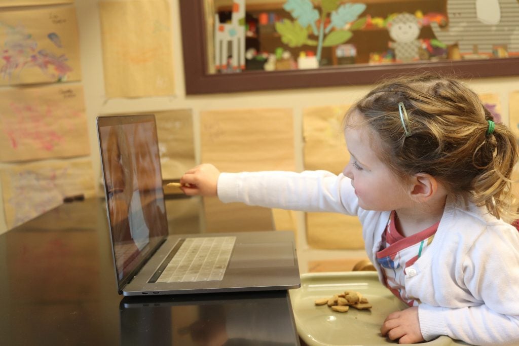 Photo of Child Reaching for computer screen where grandparents are calling in from videochat