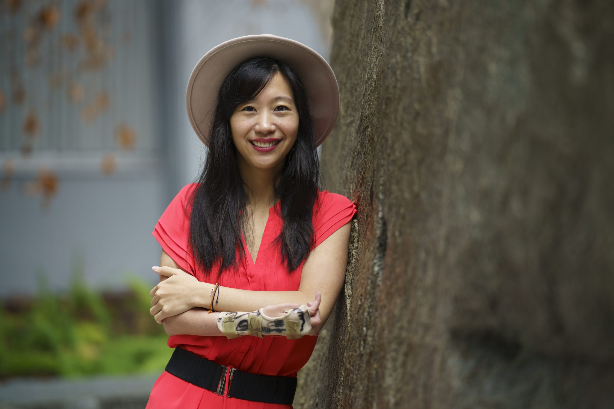 photo of Tiffany Yu in a red dress and hat leaning against a tree smiling