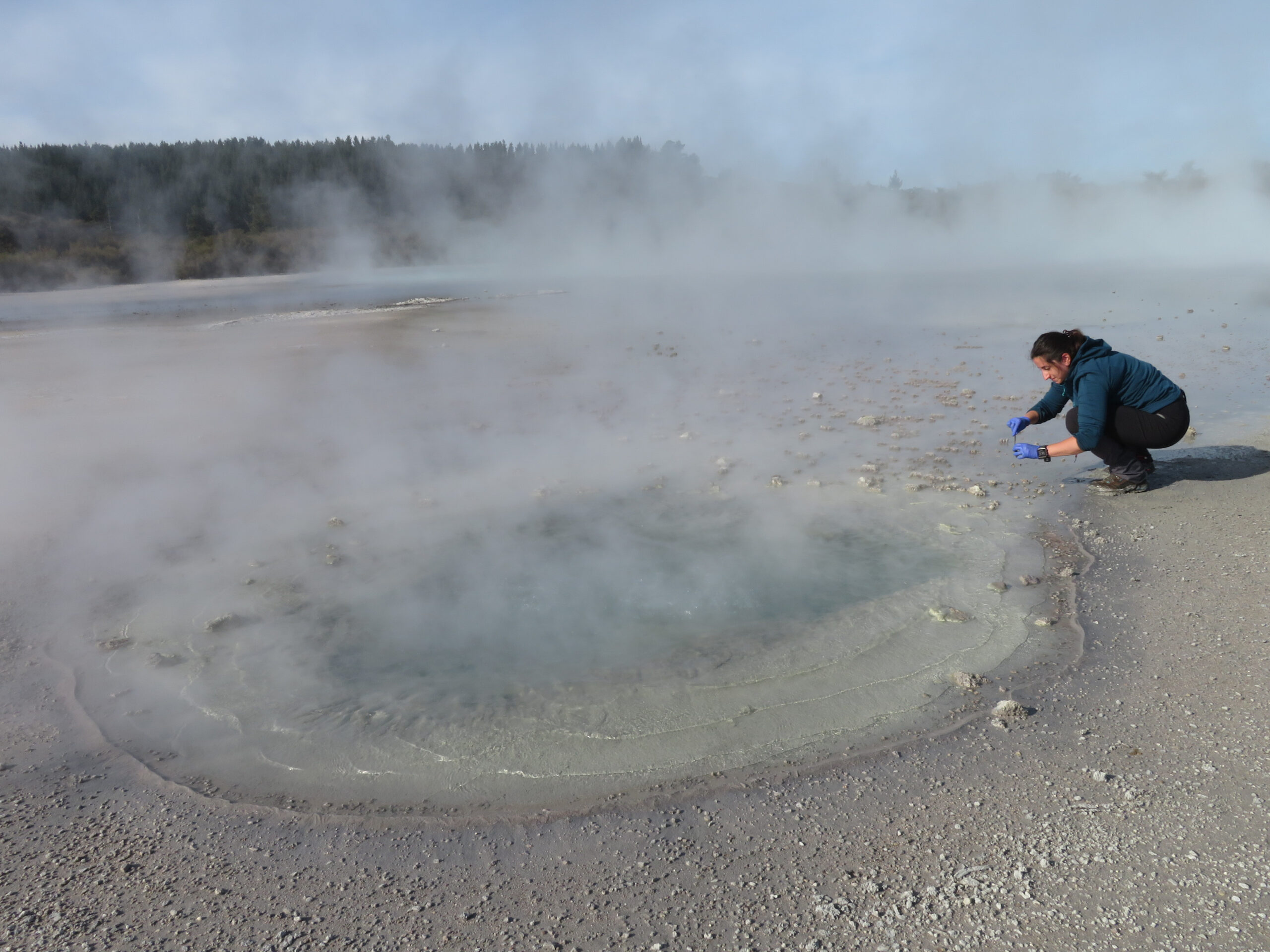 Millan crouches over New Zealand hot spring collecting sample