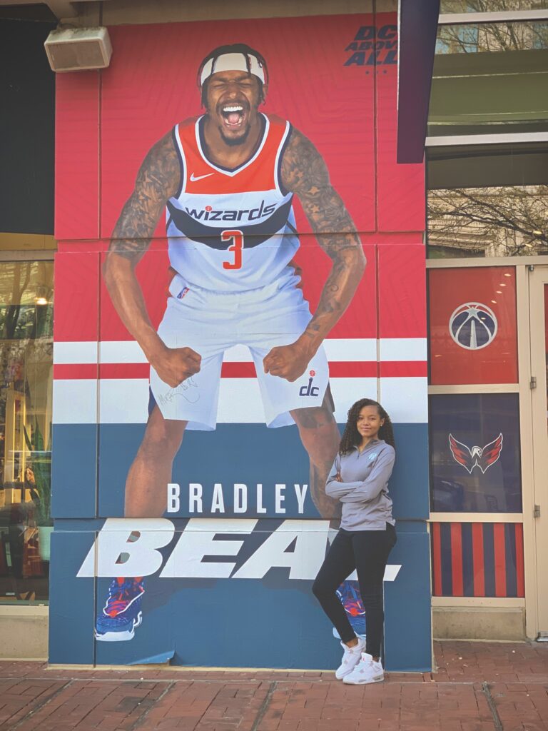Daelyn stands in front of an enormous poster of Bradley Beal in front of Capital One Arena
