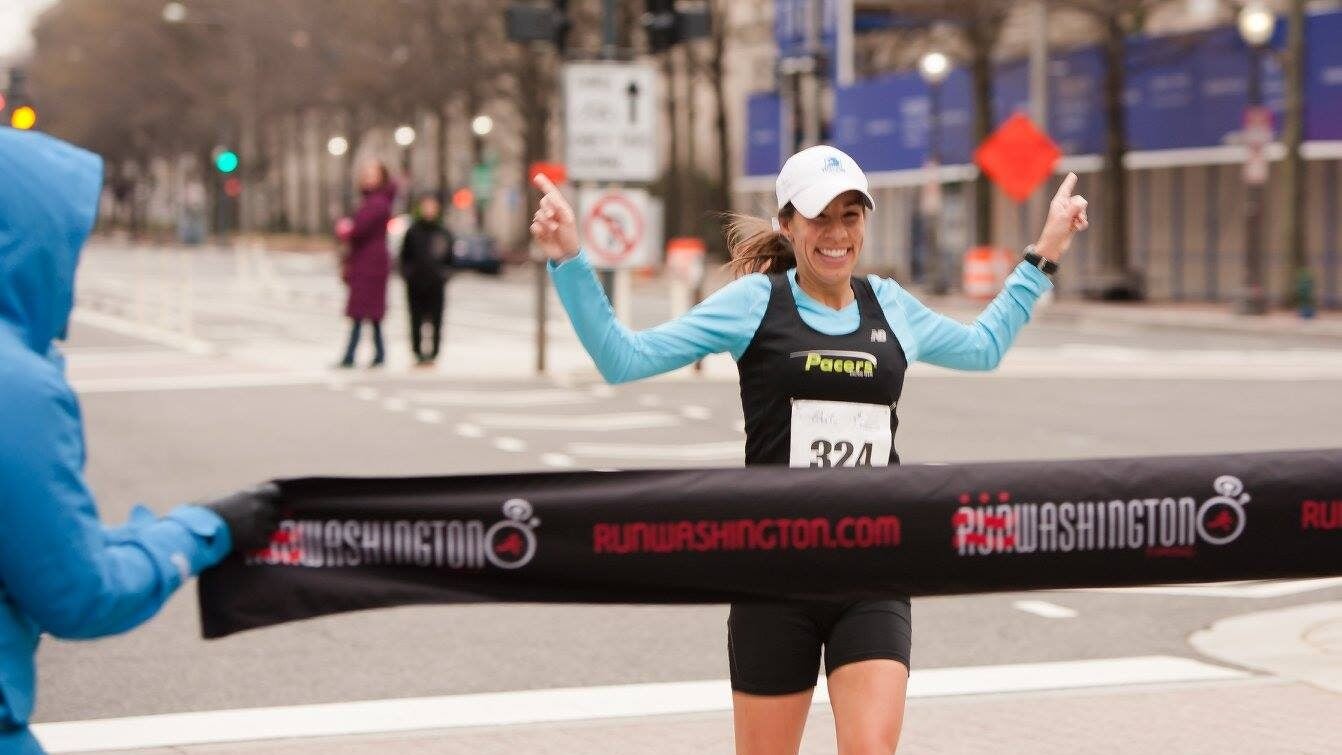 Corcoran runs with her arms in the air toward the finish line at a DC marathon.