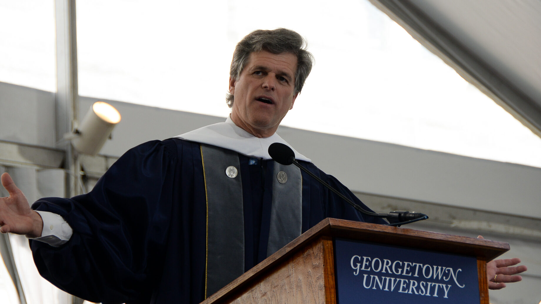 A man in academic regalia speaks at a podium.