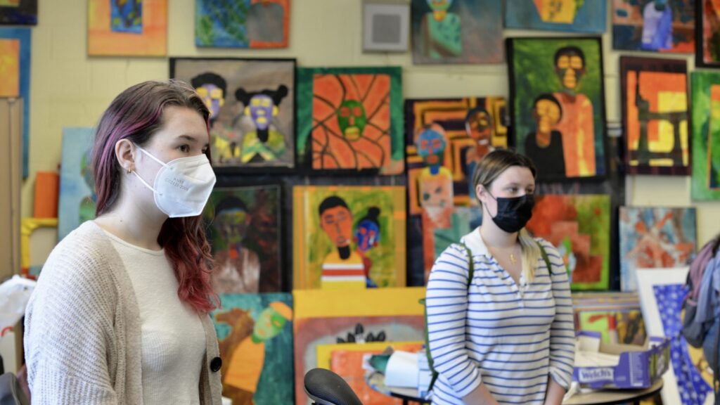 Two Georgetown students stand in front of a wall of paintings.