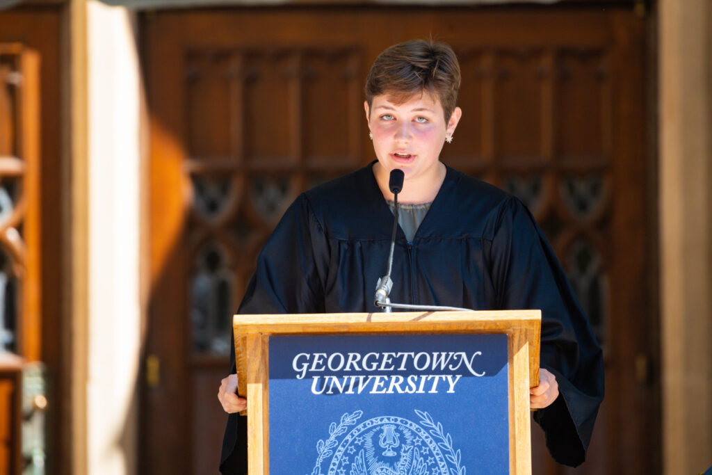 A robed woman with short hair speaks at a podium. 