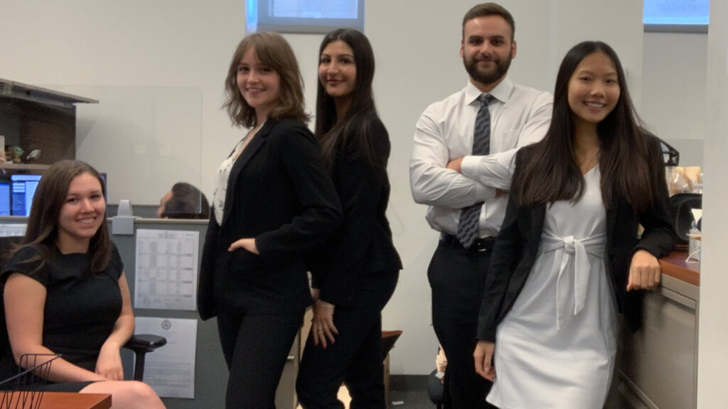 A group of interns in professional attire stands in an office.