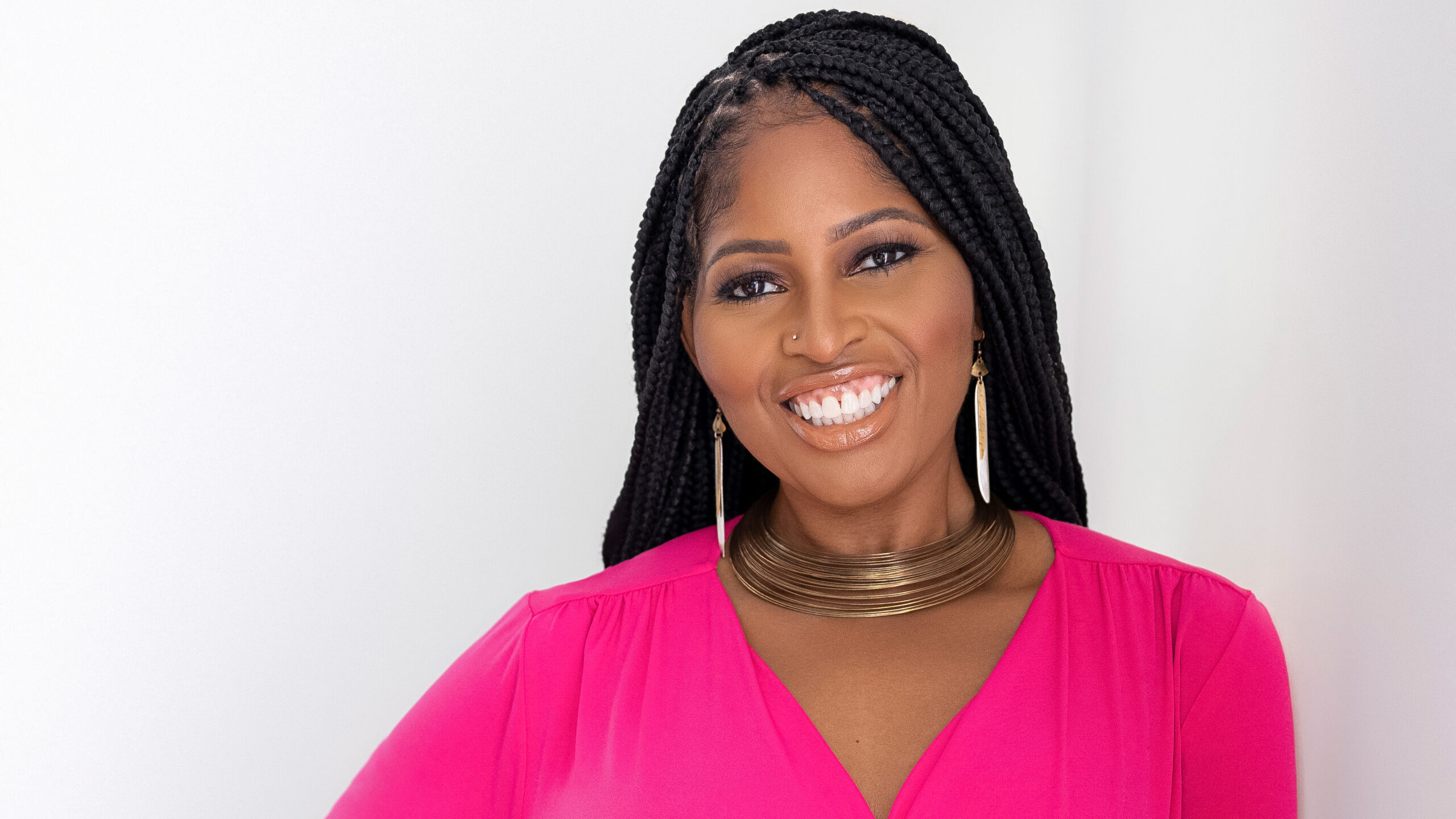 A woman with dark braids smiles in front of a white background.