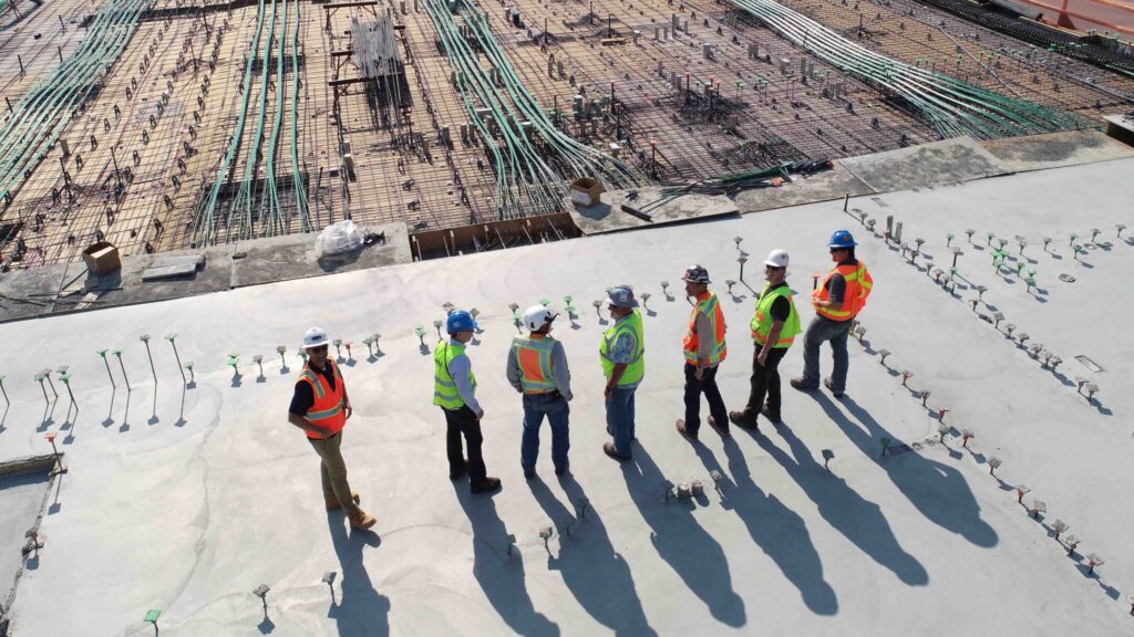 A group of construction workers in hard hats stands on a cement slab.