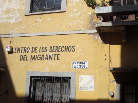 A tan building with the words Centro De Los Derechos Del Migrante painted on the exterior. 