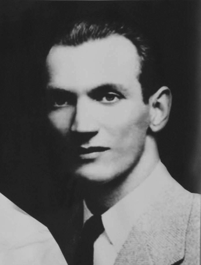 A black-and-white photo of a young man wearing a suit. His hair is combed back. 
