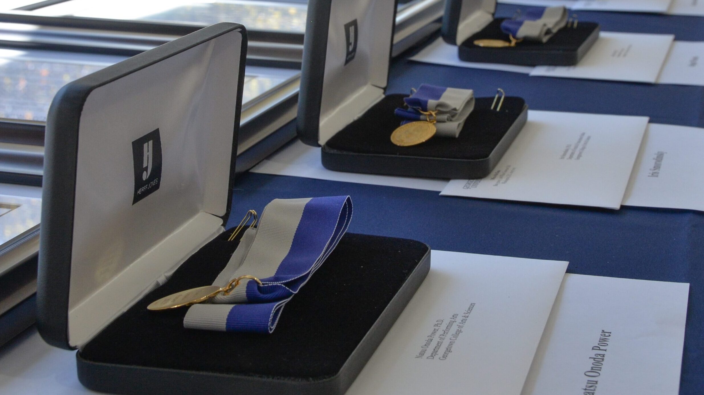 Three medals strung on blue and gray ribbons set in their cases on a table.