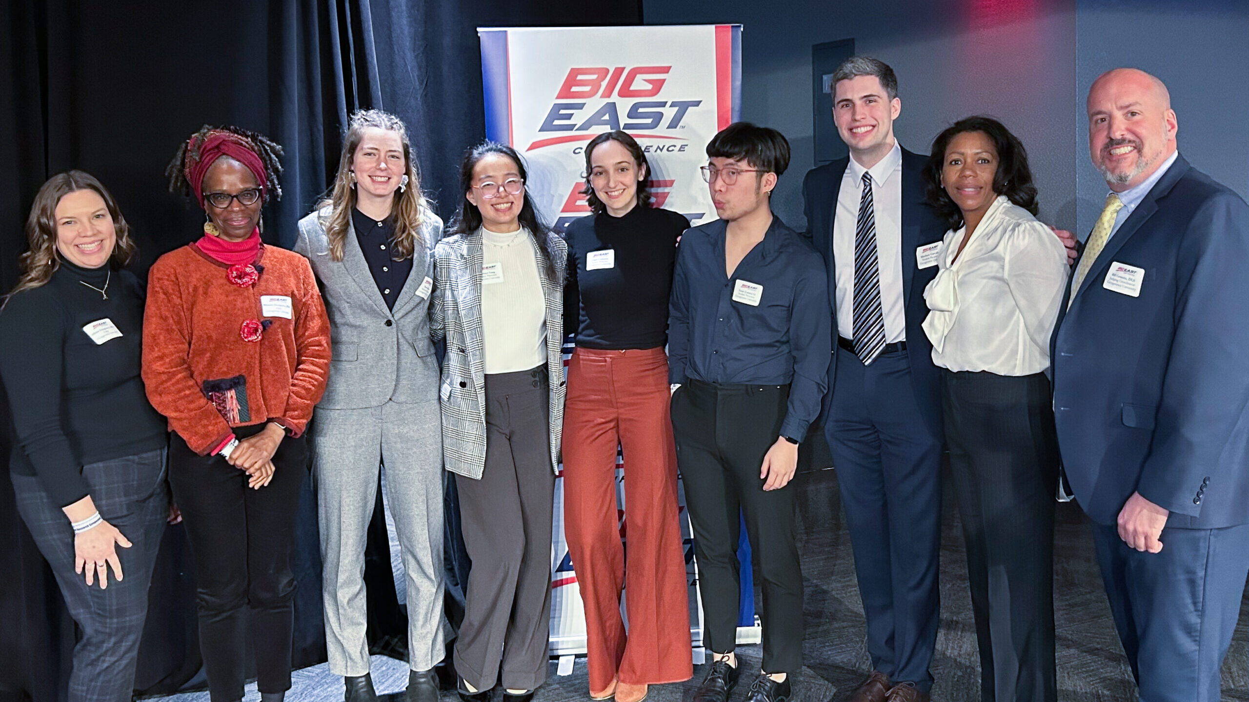 A group of students in formal attire stand in front of a Big East banner.