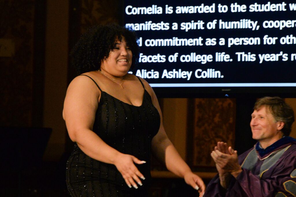 A woman wearing a black dress walking across a stage to receive an award. 