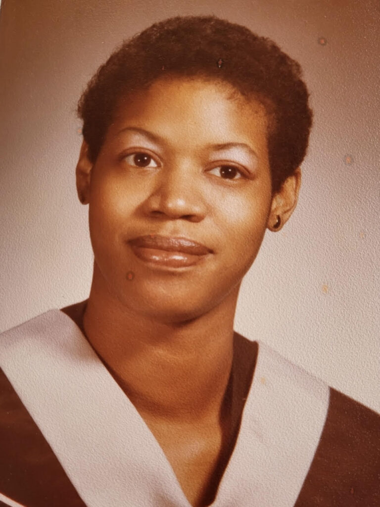 A woman with short black hair wears academic regalia. The photo is in sepia tones with small marks indicating its age. 