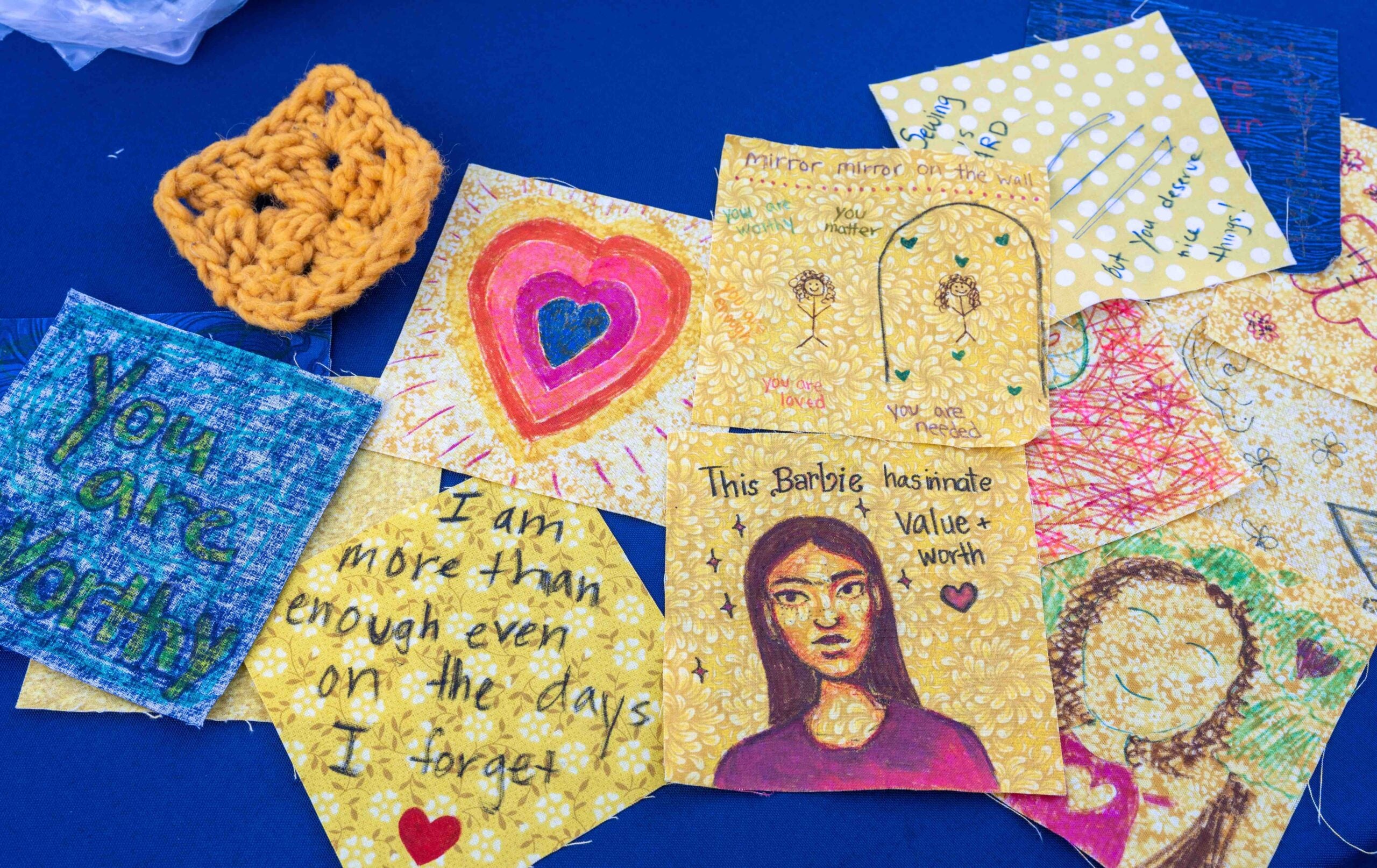 Artwork on small, square pieces of paper featuring affirmations and bold colors. The work is displayed against a bold, blue backdrop. 
