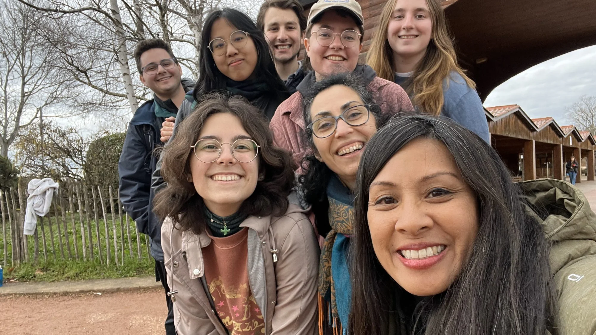 A group of students smiles in a selfie. They are outside and wearing jackets and hats.