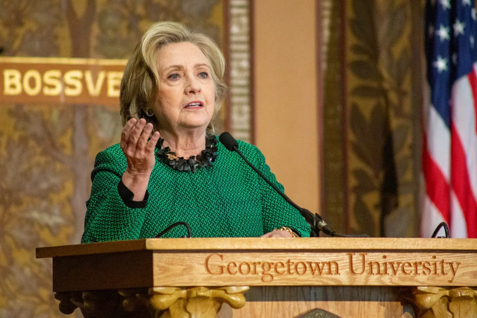 A woman in a green formal jacket speaks at a podium emblazoned with the name Georgetown University. 
