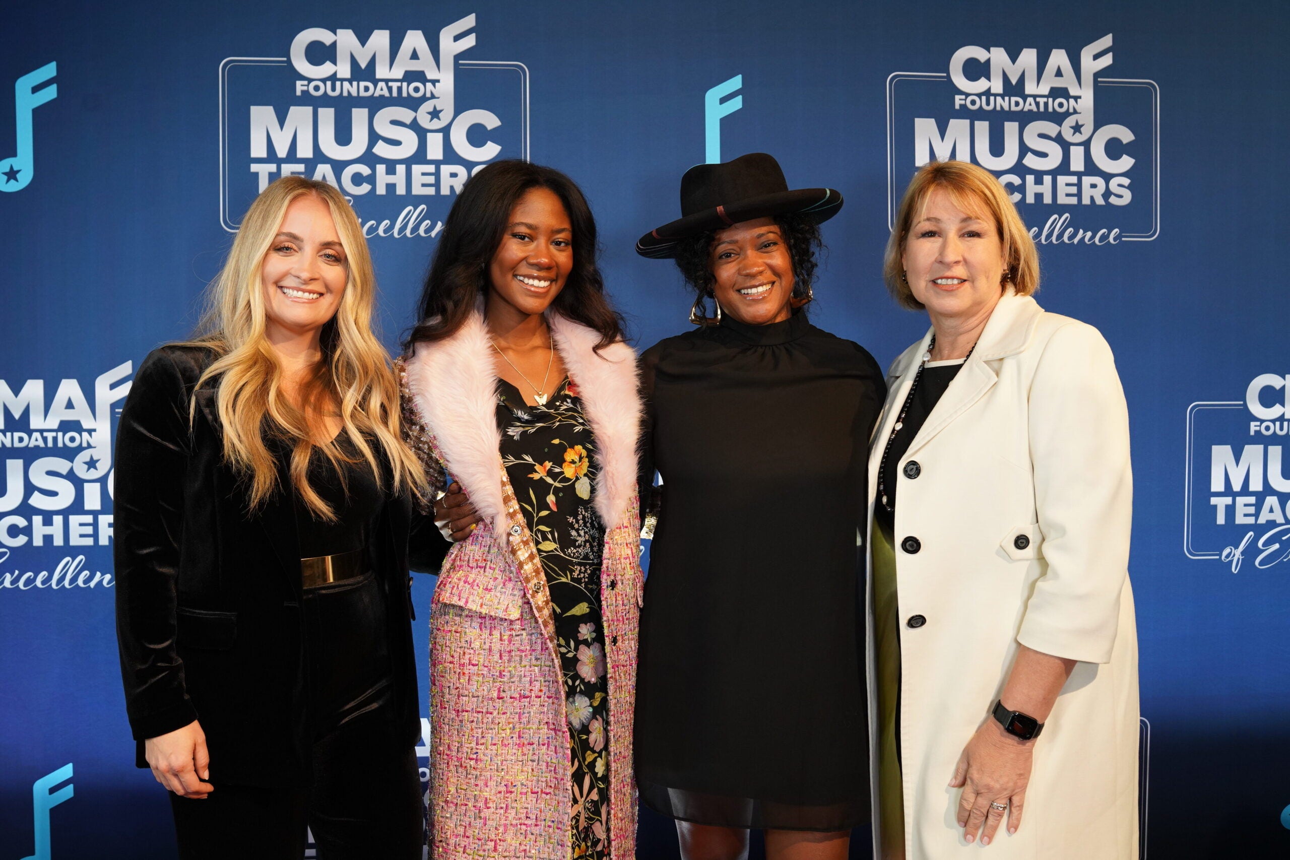 Four woman stand in front of a blue step-and-repeat for the Country Music Association.