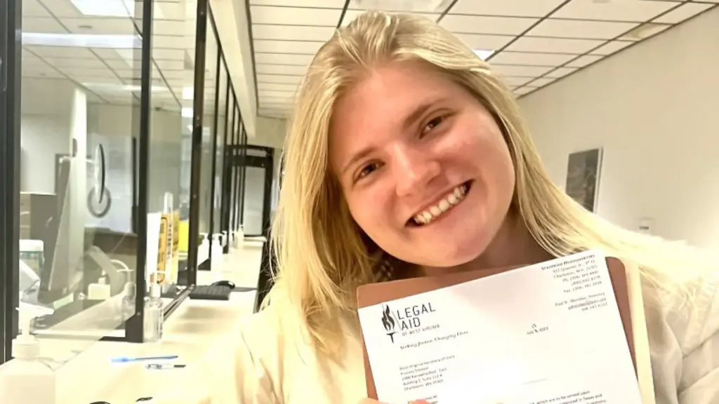 A girl with long, blonde hair smiles at the camera. She holds a paper in front of her announcing her acceptance into a legal internship. 