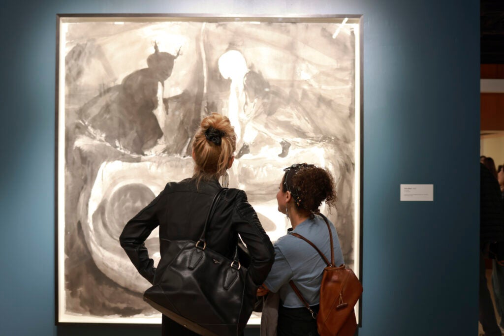 The silhouette of two women, taken from behind, looking at a piece of art work done in shades of black and white.