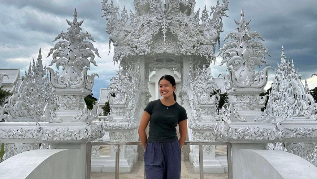 A girl with medium-length dark hair stand i front of an all-white temple.