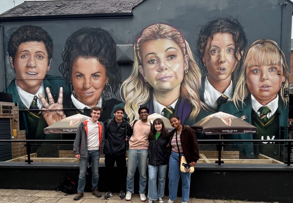 Four people stand in front of a building with a mural from a popular television show behind them.