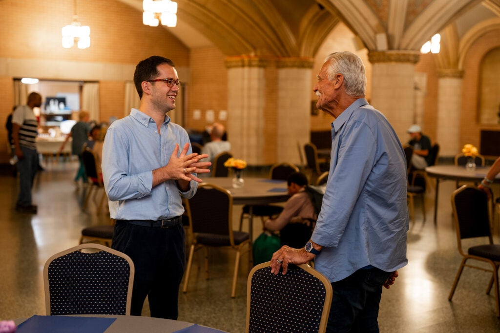 Two men, one younger and one older, talk in the community fellowship hall of a church.