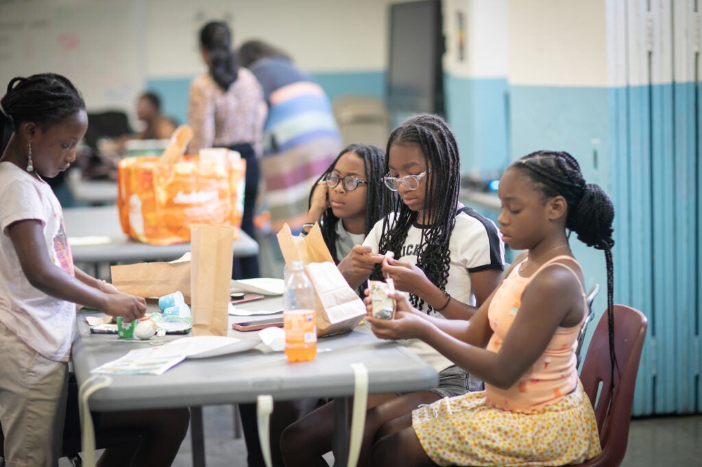 Young girls sit around a table and engage in a science experiment.