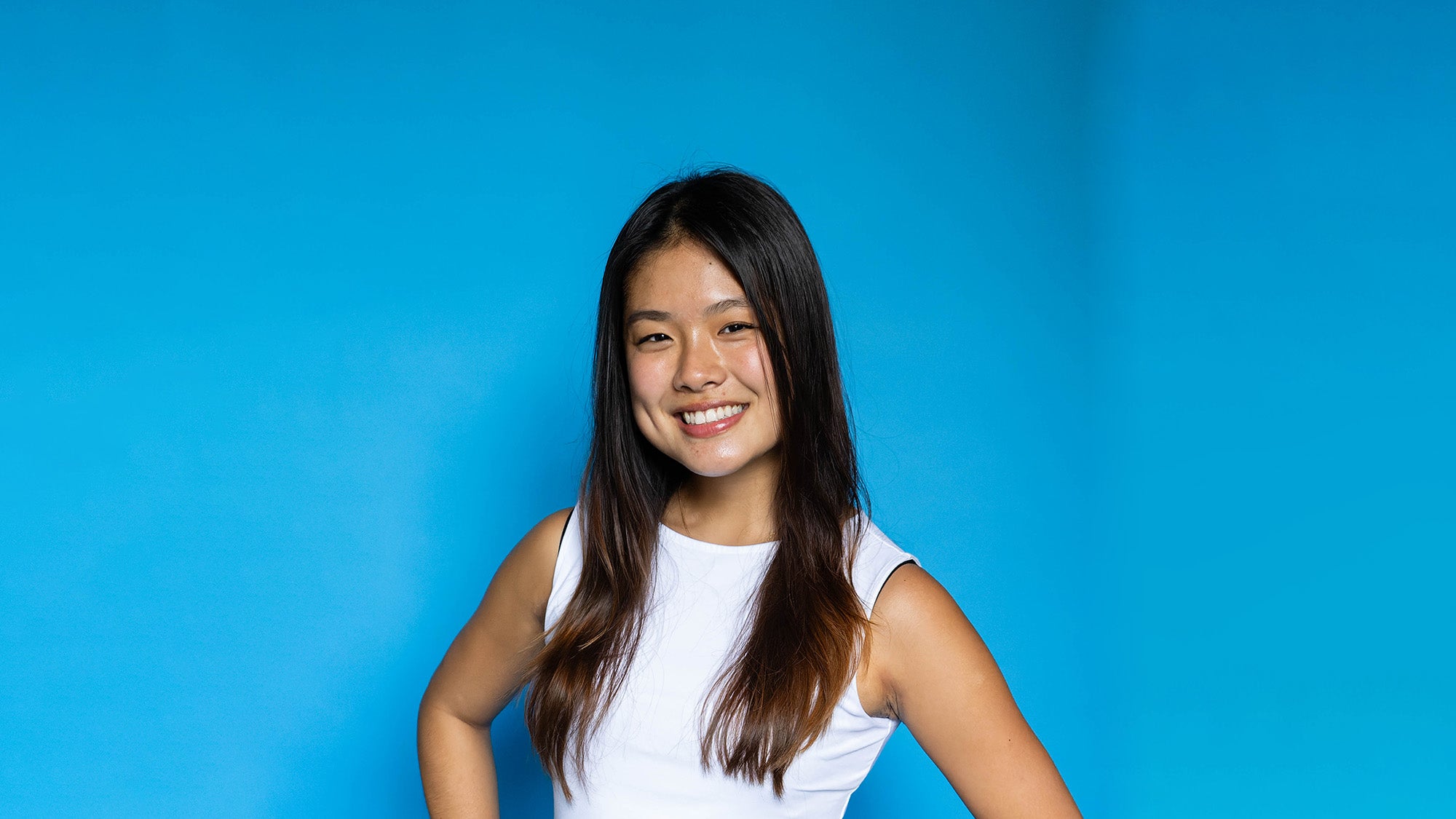 A girl with long dark hair smiles in front of a blue background.