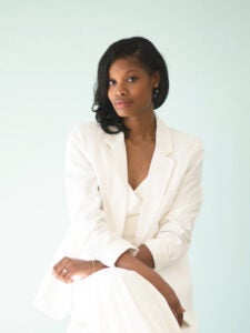 A woman in all white sits and poses for a portrait. She has medium-length dark hair. 