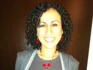 A woman with medium-length curly black hair smiles inside. 