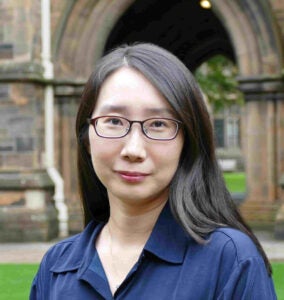 A woman with long, dark hair smiles outside. She wears a blue blouse. 