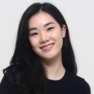 A girl with long dark hair smiles in front of a white background. 