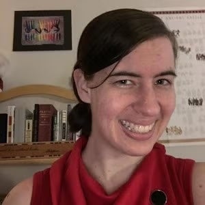 A woman with her hair in a ponytail smiles at the camera. She wears a red blouse. 