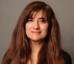 A woman with medium-length auburn hair smiles softly in front of a neutral background.