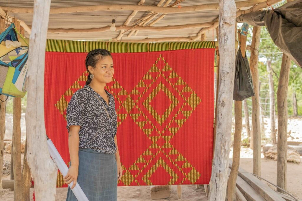 A girl with her hair in a braid stands outside. Behind her is a piece of red fabric.