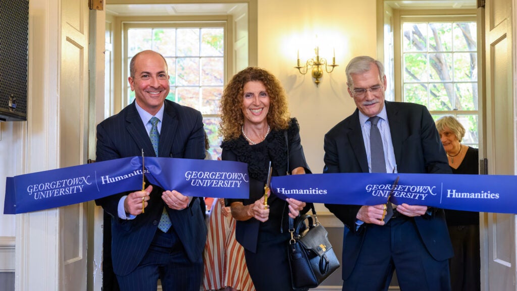 Three people in formal attire use scissors to cut a ceremonial ribbon.