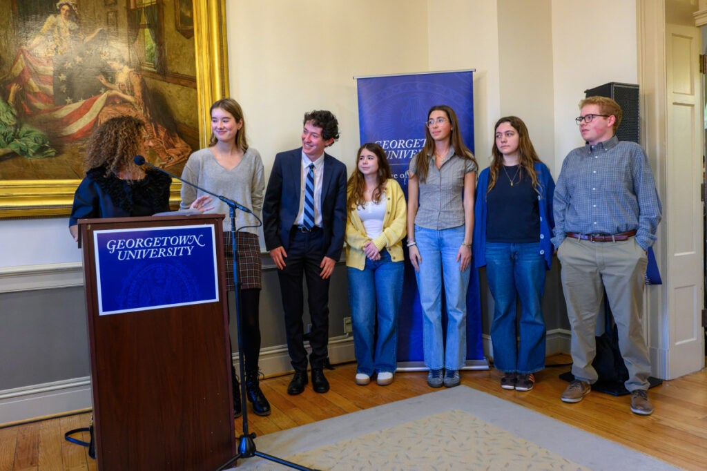 A group of students stand behind a podium. 