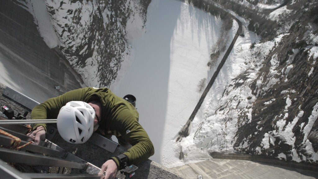 A man wearing a helmet climbing a 600-foot dam in Switzerland.