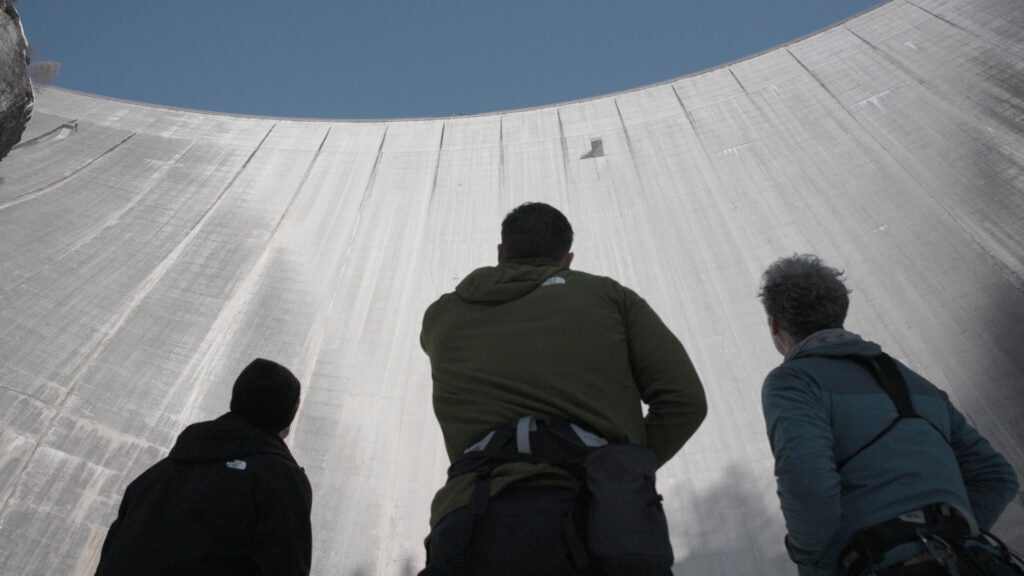 Three people looking up at the Luzzone dam in Switzerland.