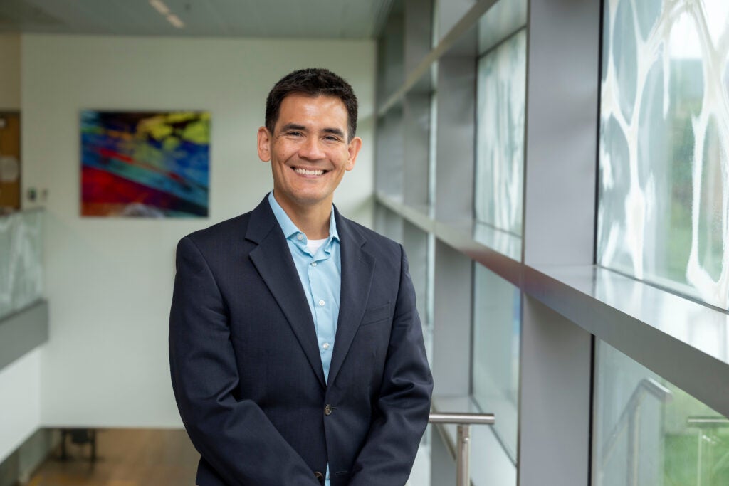 A male professor standing inside a Georgetown University building, wearing a blazer and smiling.
