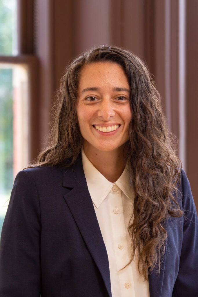 A professor wearing a white shirt and blue jacket smiling at the camera.