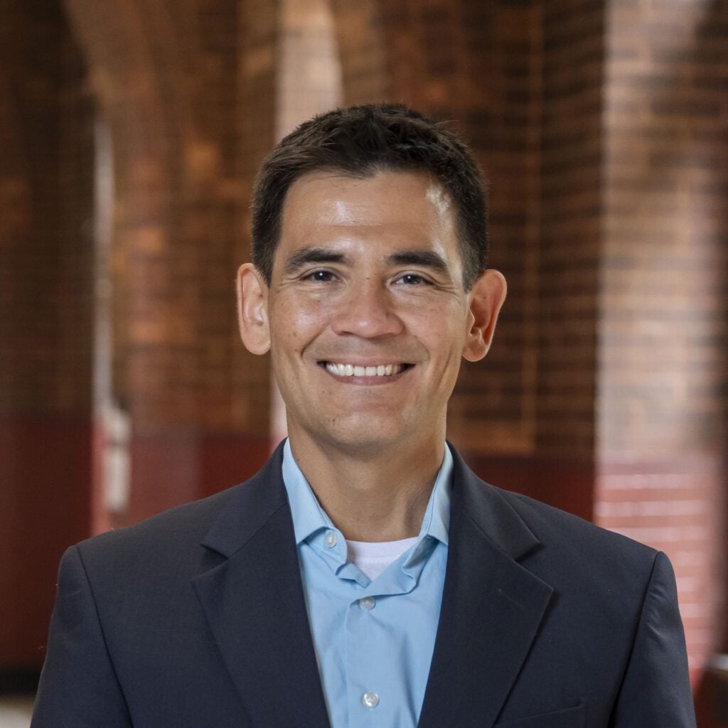A professor wearing a dress shirt and jacket smiling at the camera.