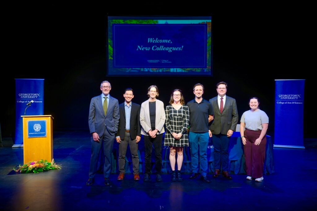 A group of staff members stand on stage smiling during a convocation ceremony.