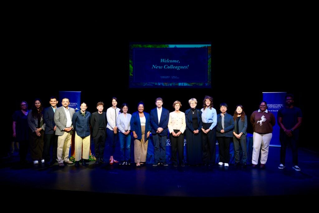 A group of faculty members stand on stage smiling during a convocation ceremony.