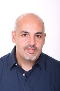 A professor wearing a blue collared shirt looking at the camera for a headshot.
