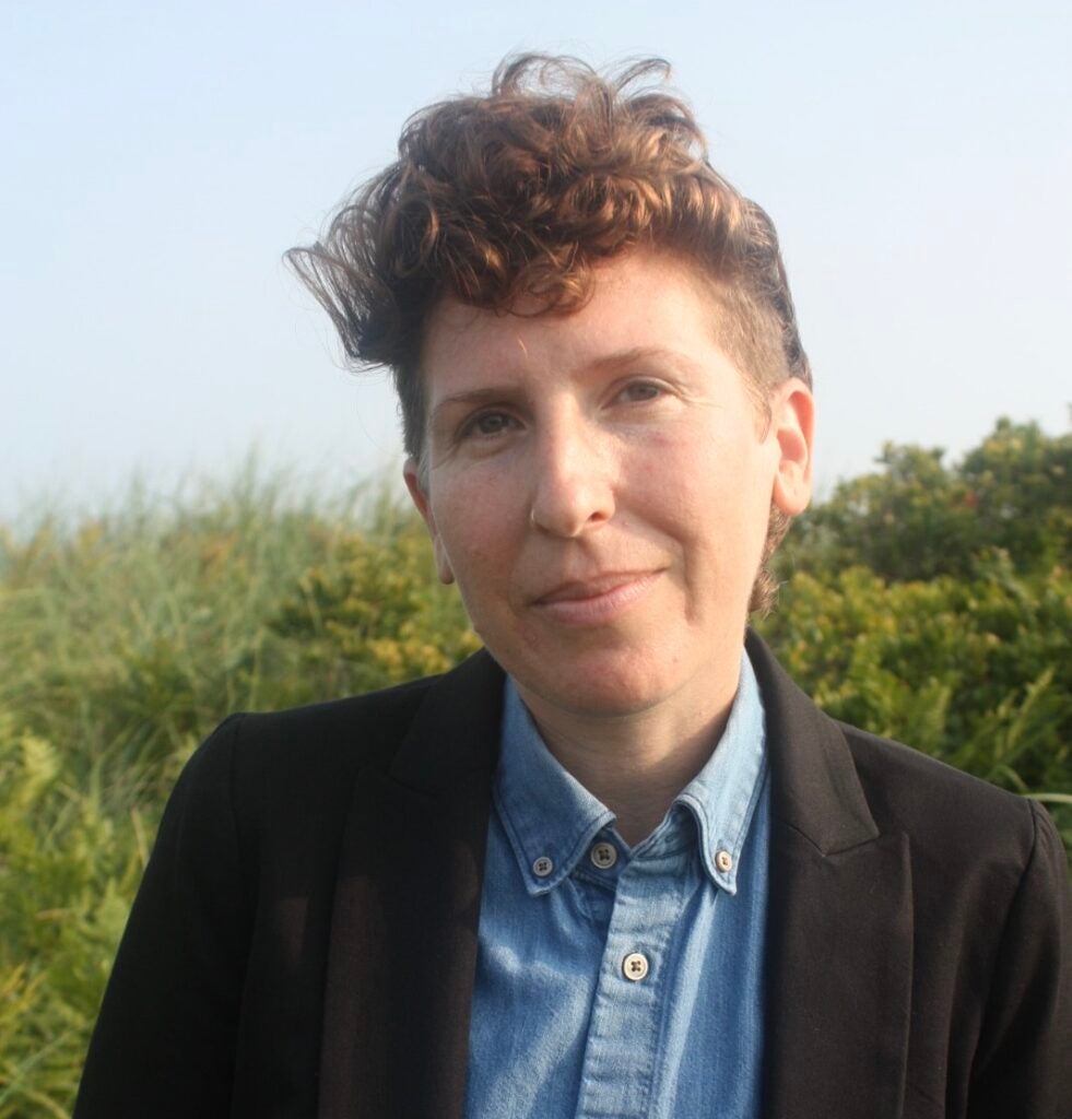 A professor wearing a blue shirt and black jacket smiling at the camera.