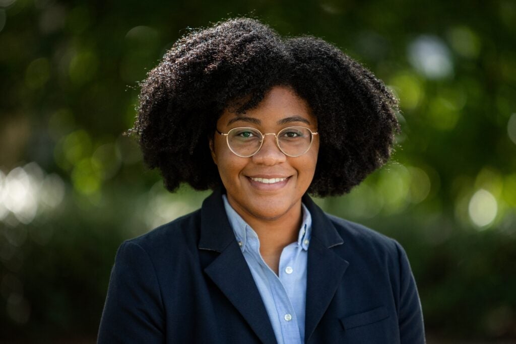 Headshot of a smiling professor with glasses in a light blue shirt and dark blue jacket.